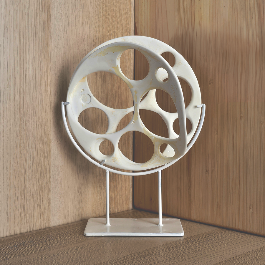 A white decorative geometric sculpture on a matching white stand, displayed against a light wood paneled background and countertop.