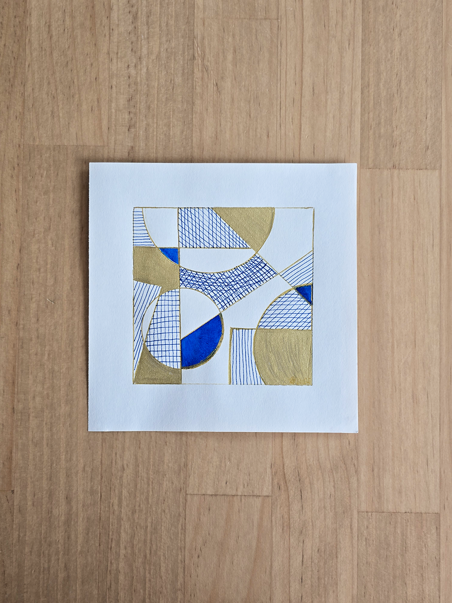 An abstract geometric art print featuring blue, gold, and white shapes with hatched and striped patterns, displayed on a light wood countertop.