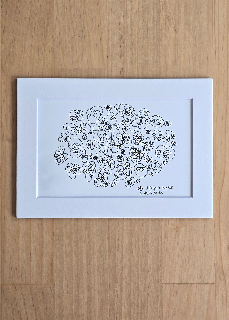 A black ink abstract drawing of intuitive circular and looping shapes on white paper inside a white mat, displayed against a light wood background.