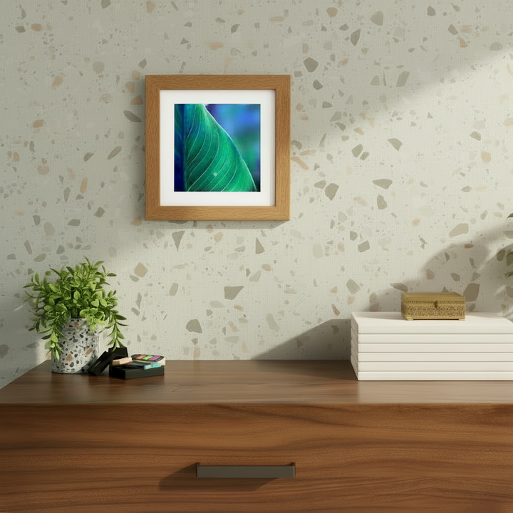 Framed abstract macro photography of a green leaf by Ava Bock displayed on a textured neutral wall above a wood console in a modern interior setting.