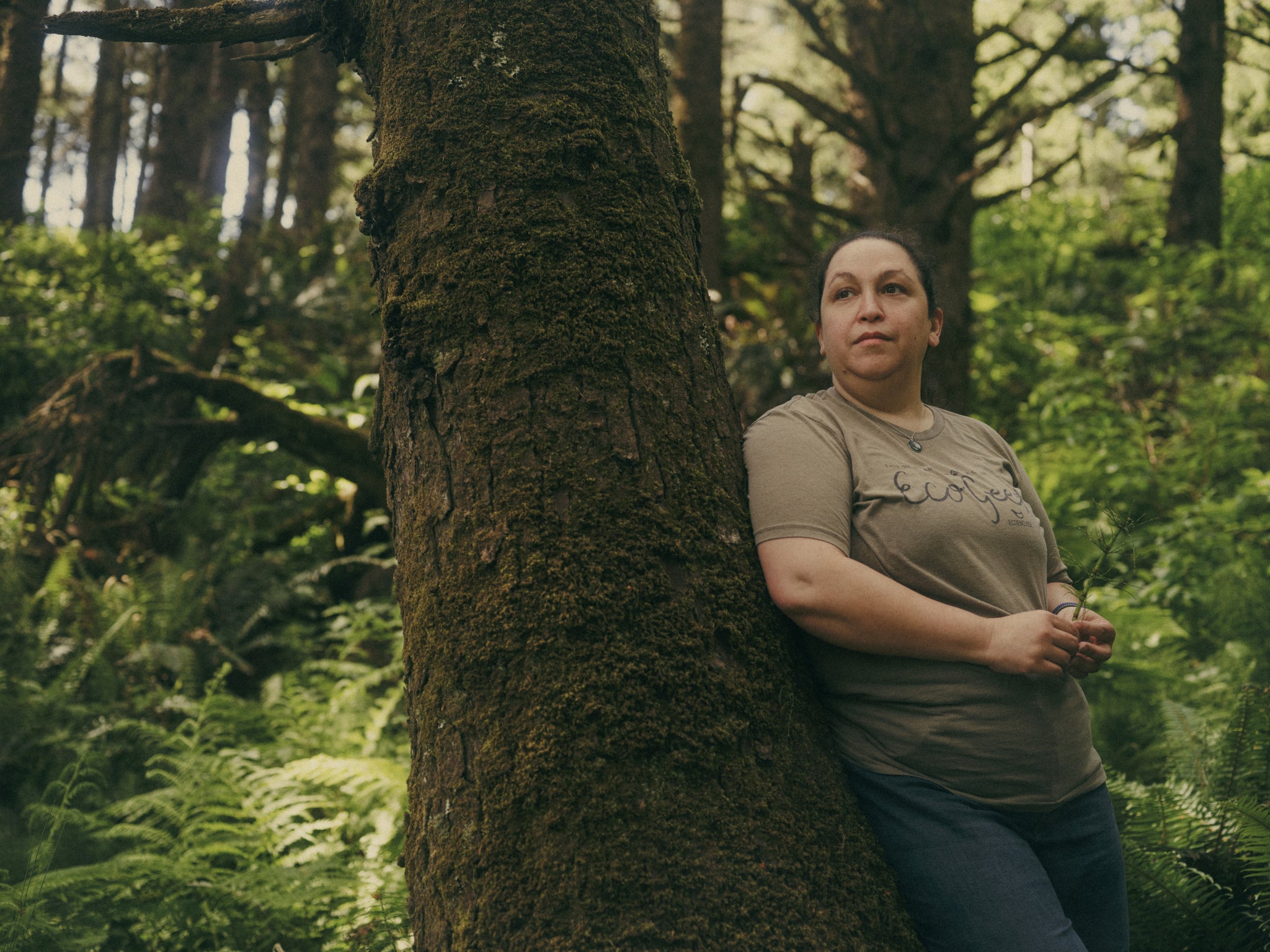 Artist Ava Bock standing beside a tree in a forest environment reflecting the environmental values that inform her art practice.